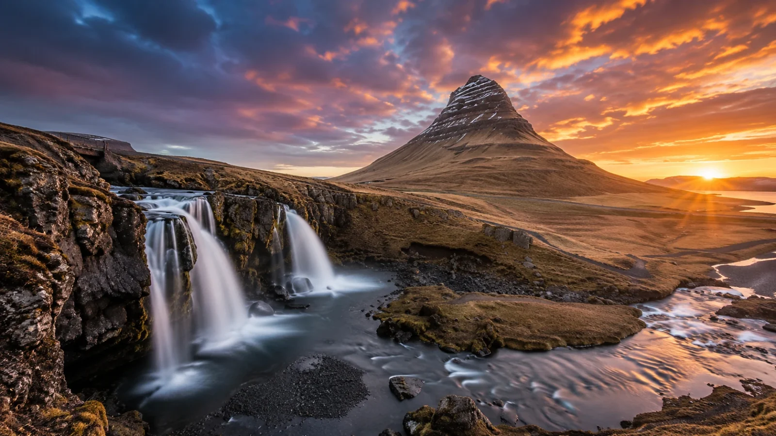 Kirkjufell mountain and Kirkjufellsfoss waterfall in Iceland beneath a dramatic sunset sky.