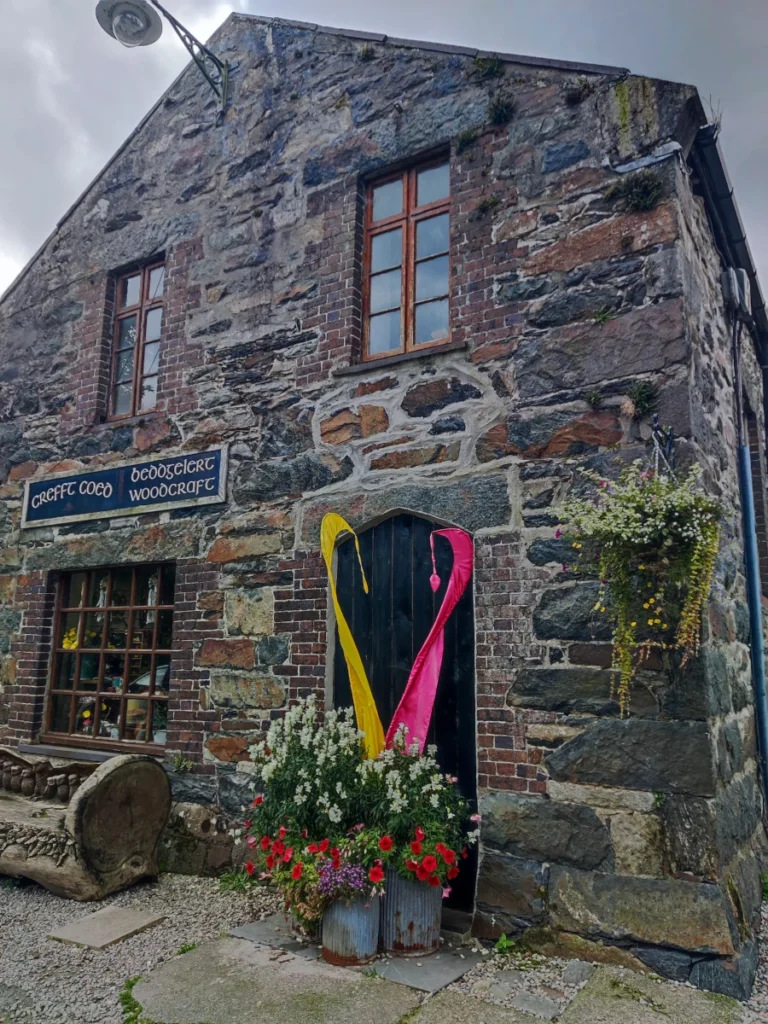Beddgelert Woodcraft shop front in a traditional stone building with hanging flower baskets