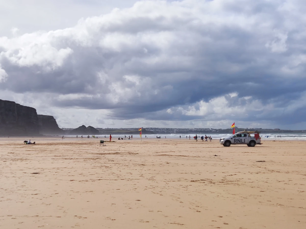 Wide sandy beach at Perranporth, Cornwall, with cliffs, an RNLI lifeguard vehicle, and dramatic clouds