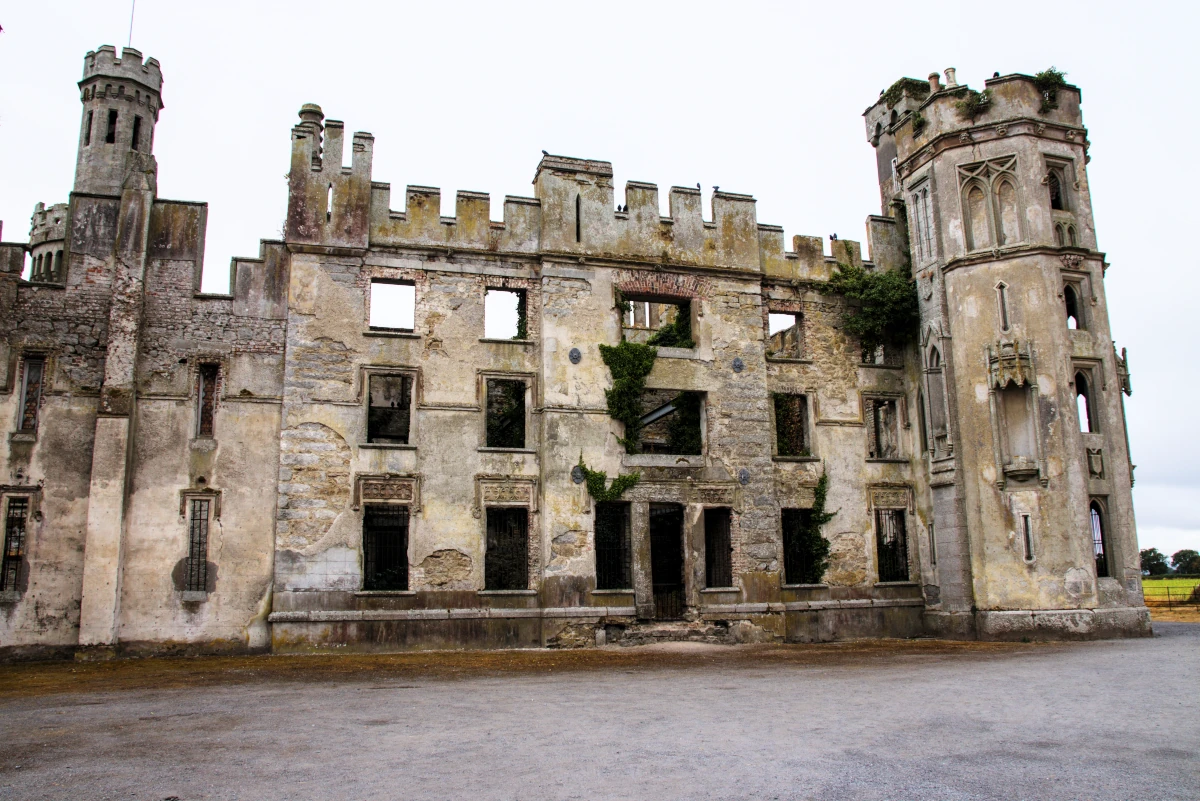 Close-up of Duckett's Grove's ruined Gothic Revival facade with empty windows, ivy, and twin towers in County Carlow, Ireland