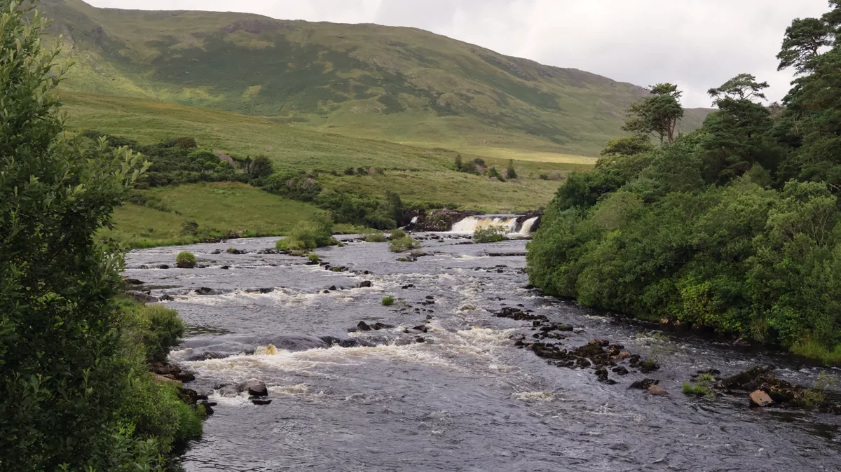 Closer view of Aasleagh Falls, a wide low waterfall on the River Erriff, with rocks in the river and green hillside behind, County Mayo, Ireland