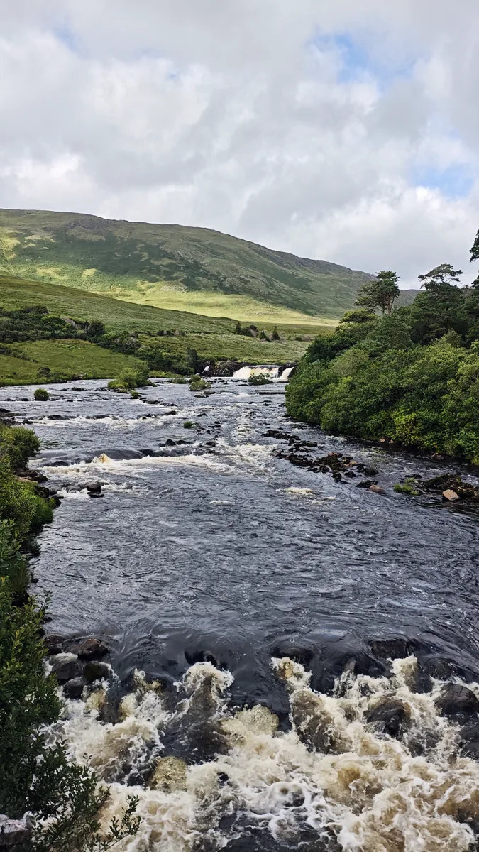 Rapids on the River Erriff in the foreground with Aasleagh Falls in the distance and sunlit green hills, County Mayo, Ireland