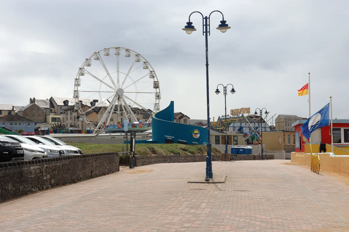 The white Ferris wheel and funfair rides of Bundoran Adventure Park behind the paved seafront promenade in Bundoran, County Donegal, Ireland