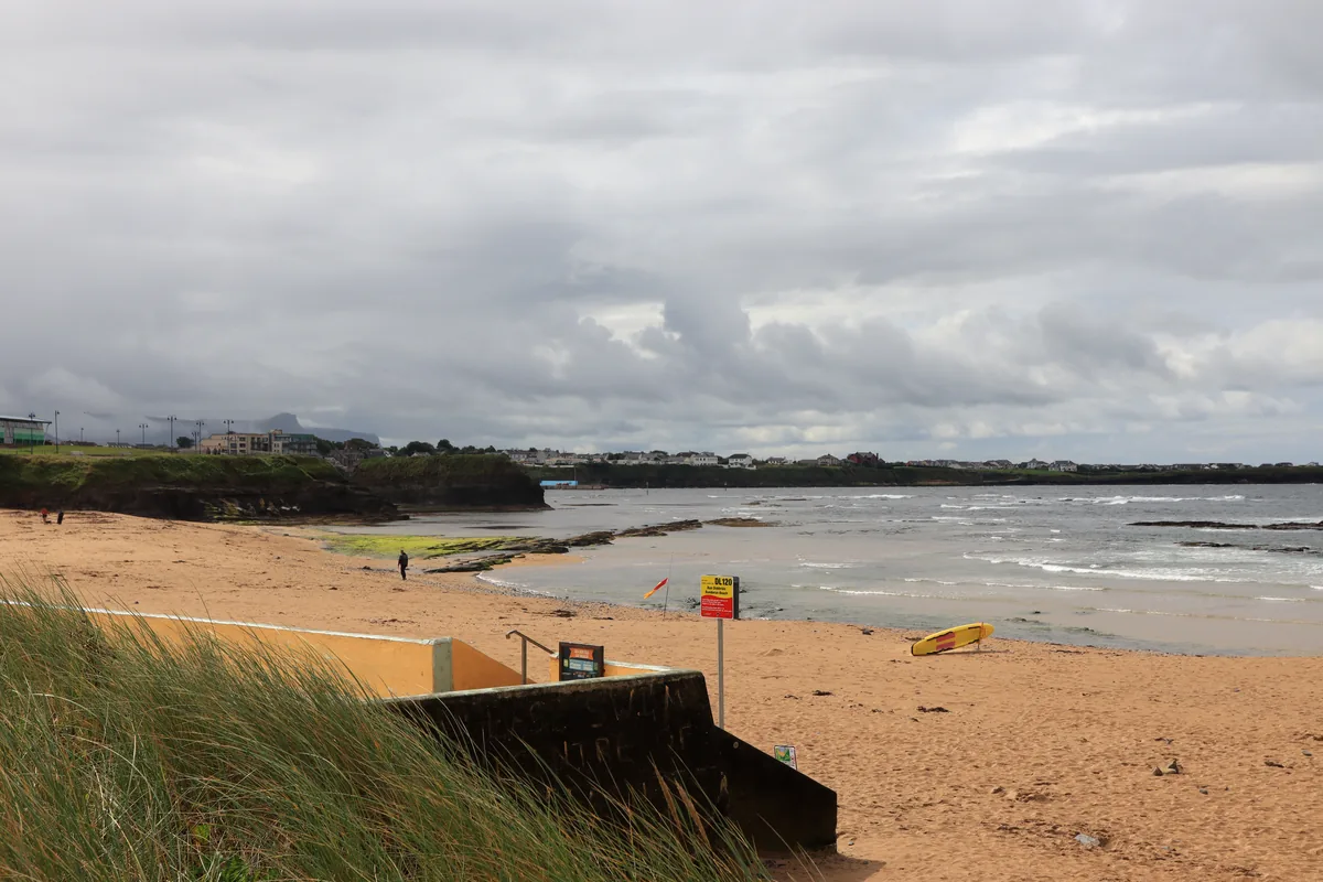 Beach access steps, a Bundoran Beach information sign, a lifeguard flag and a yellow rescue board on the sand in County Donegal, Ireland