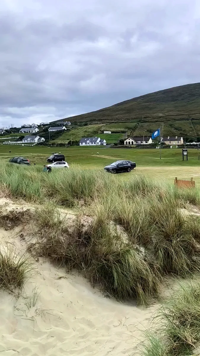 Blue Flag flying above the grass parking field at Dugort Beach, Achill Island, with cars, houses and the slopes of Slievemore