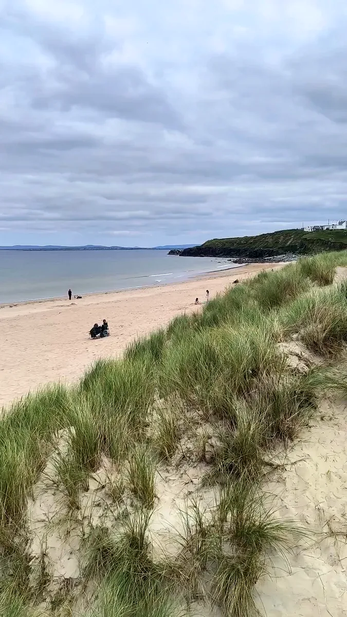 Sandy Dugort Beach on Achill Island, Co. Mayo, seen from the marram grass dunes on a cloudy day, with a few visitors on the sand