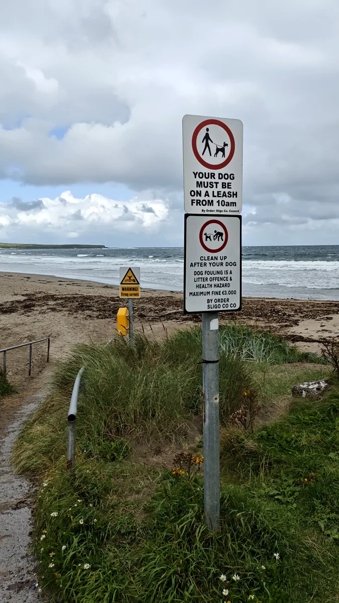 Signs at Dunmoran Beach, Co. Sligo: dogs must be on a leash from 10am, clean up after your dog, and a warning about strong currents.