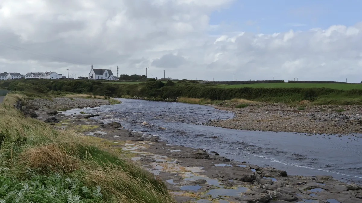 River flowing over rocks towards the sea at Easkey, County Sligo, Ireland, with the white village church in the background.