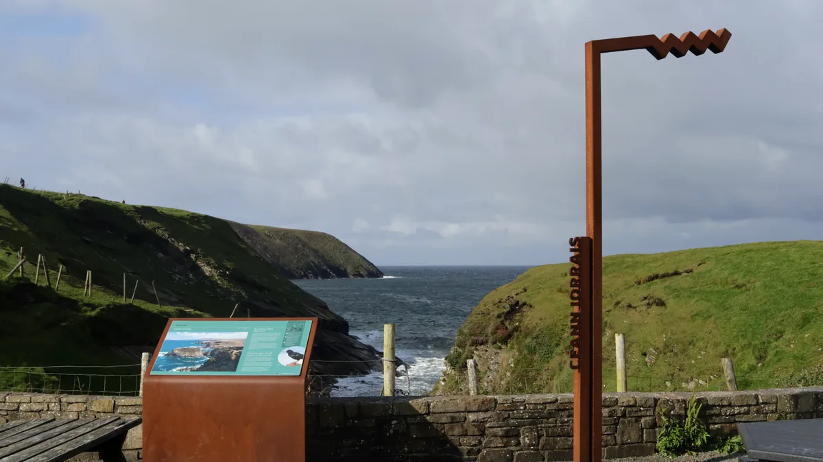 Erris Head car park in County Mayo, Ireland, with a rust-coloured "Ceann Iorrais" marker, an information panel and a view to the sea.