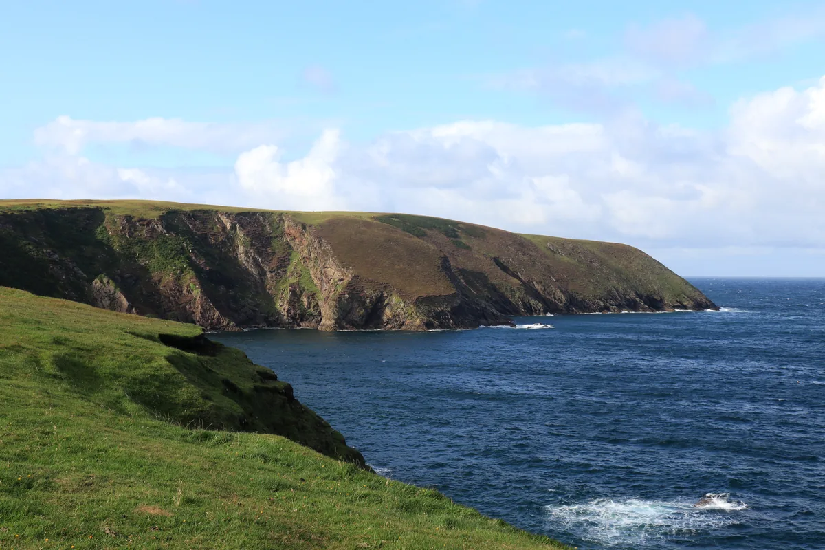 View from the Erris Head Loop Walk in County Mayo, Ireland: a grassy slope dropping to the Atlantic with a long headland of cliffs behind.