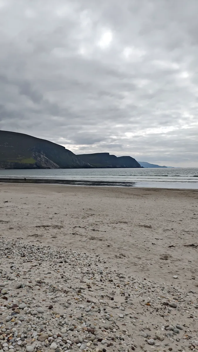 Keel Beach on Achill Island, Co. Mayo, with pebbles in the foreground and the Minaun Cliffs across the bay under grey clouds