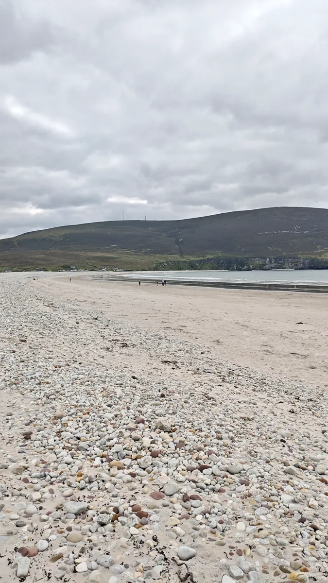 Stony upper shore of Keel Beach on Achill Island, Co. Mayo, covered in pebbles, with the sandy beach and hills behind