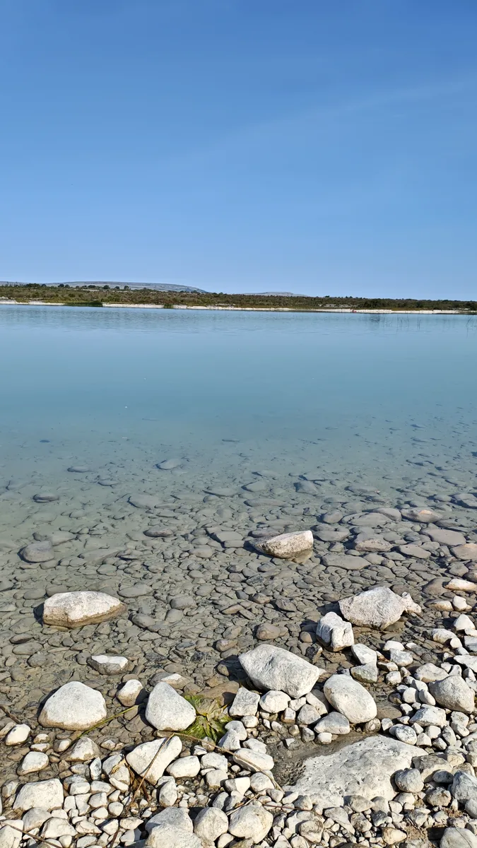 Close view of clear shallow water at Lough Bunny in the Burren, Ireland, with rounded limestone stones visible on the lakebed