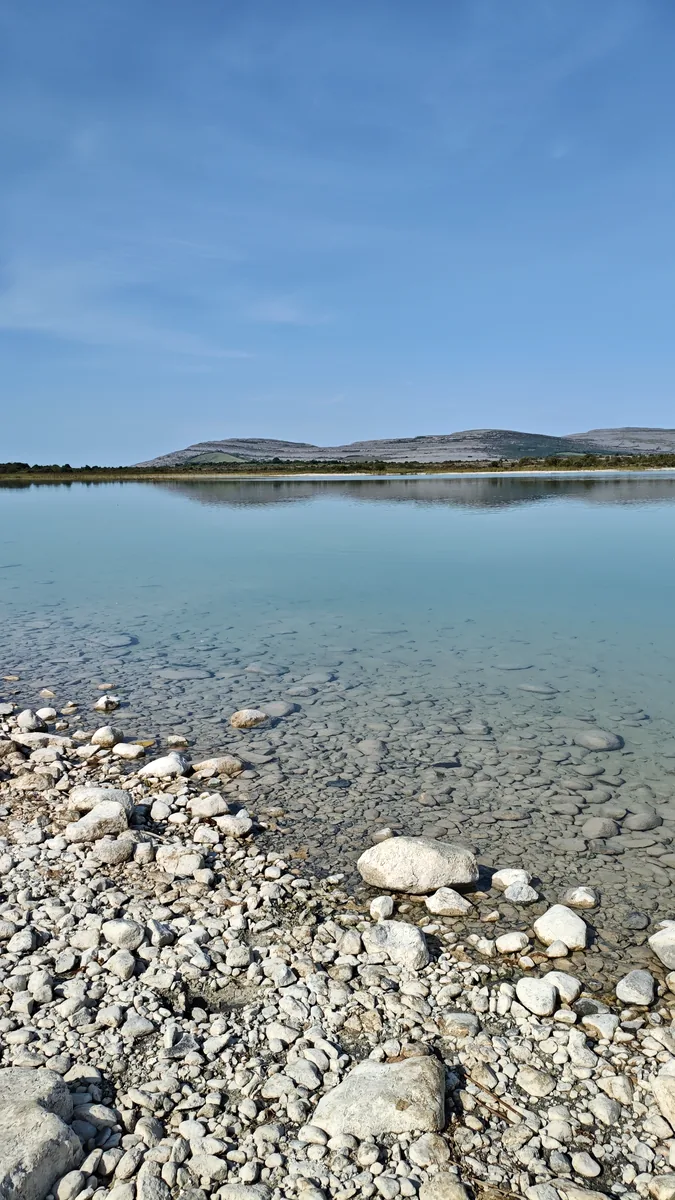 Lough Bunny in Burren National Park, Ireland, with clear water over pale stones and the limestone hills of Mullaghmore reflected in the lake