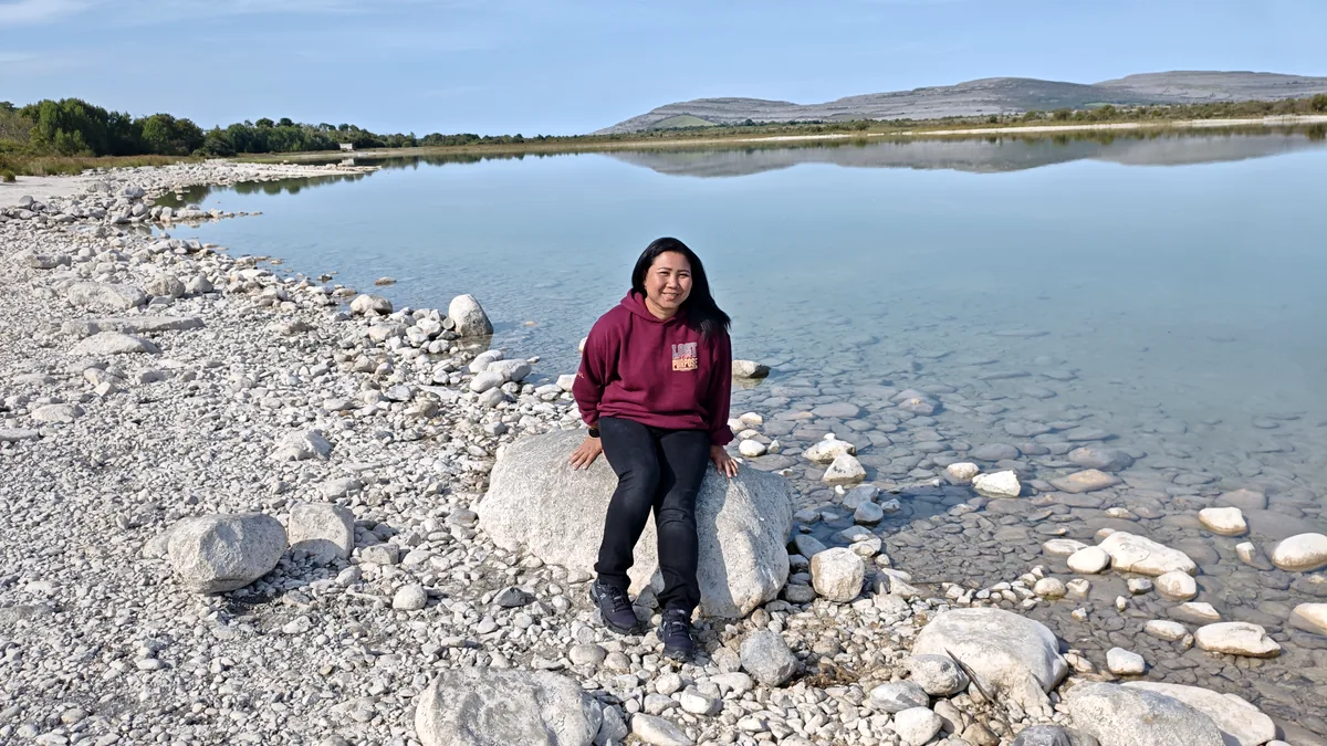 A member of THE OVRTLND team sitting on a limestone boulder at Lough Bunny, Co. Clare, with clear water and Mullaghmore behind