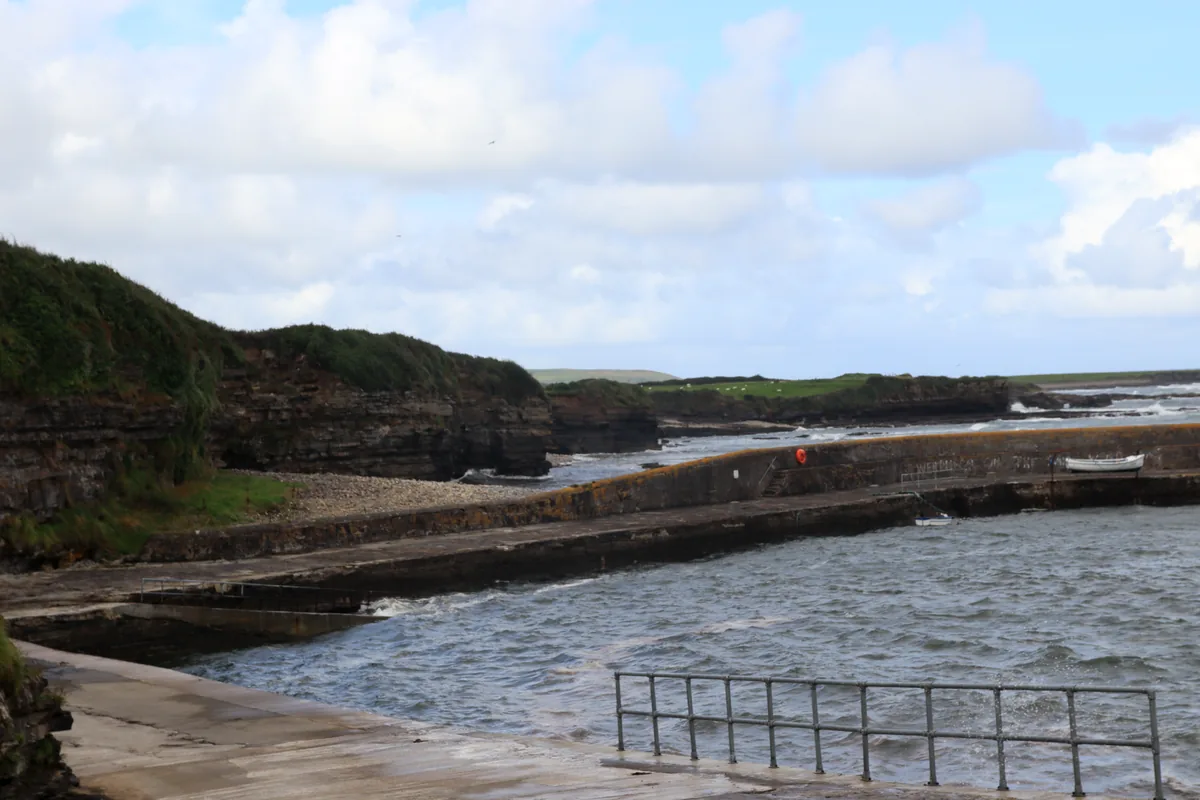 Pollnadivva Pier in Co. Sligo: the stone harbour wall with a small white boat, a slipway with railings and choppy water in front.