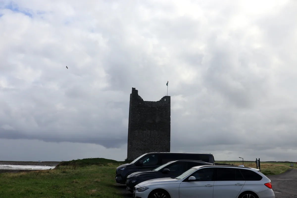 Roslee Castle car park in Easkey, County Sligo, Ireland, with three vehicles parked directly in front of the stone tower.