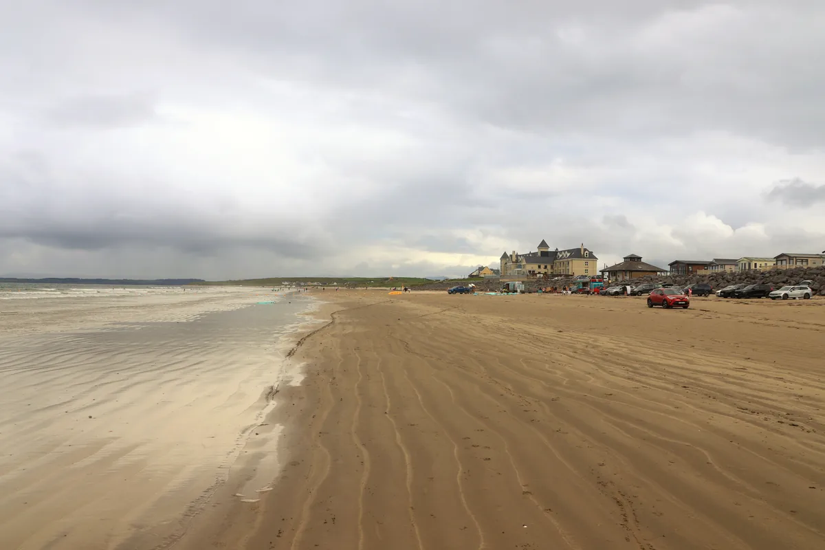 Rossnowlagh Beach in Donegal with rippled sand, the shoreline on the left and cars parked on the beach below the hotel