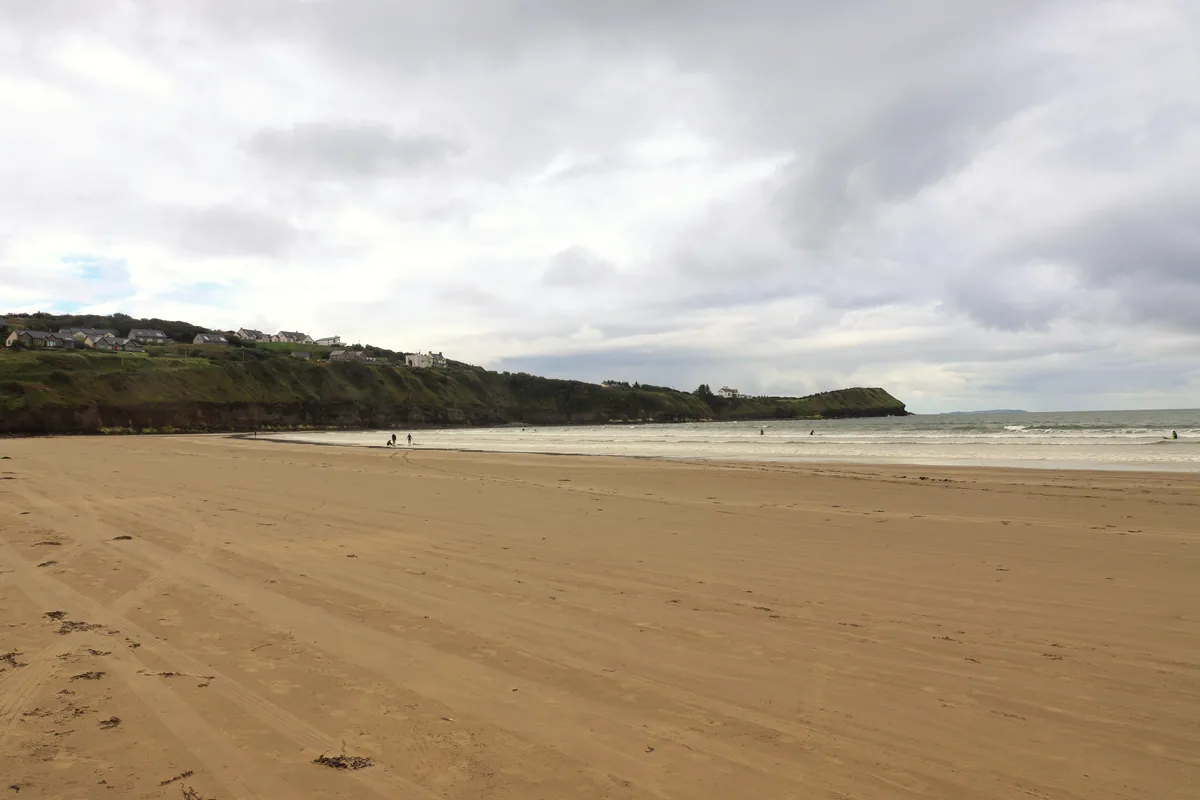 Rossnowlagh Beach in County Donegal with wide sand, surfers in the waves and the green Coolmore cliffs in the background